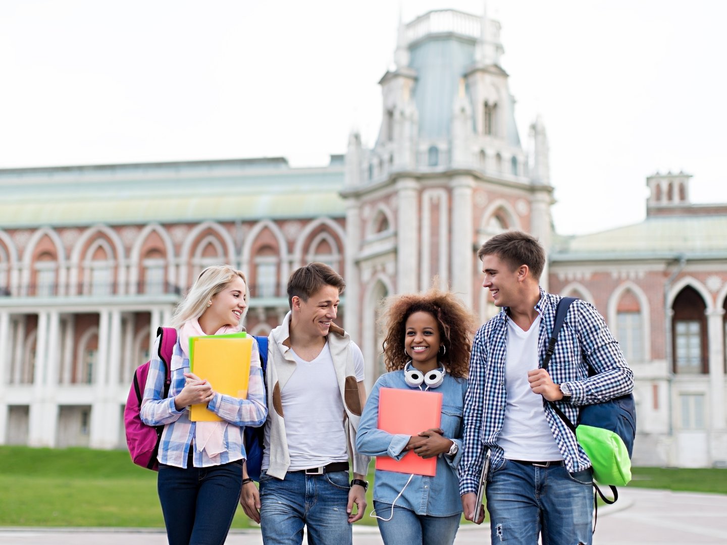 Four happy students walking together in front of a historic University campus